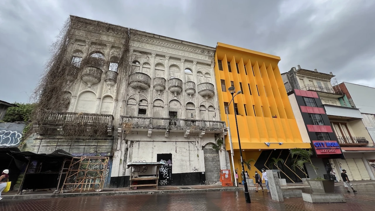 Ein graues Haus, halb verfallen mit Pflanzenbewuchs, daneben ein knallorangen modernes Haus